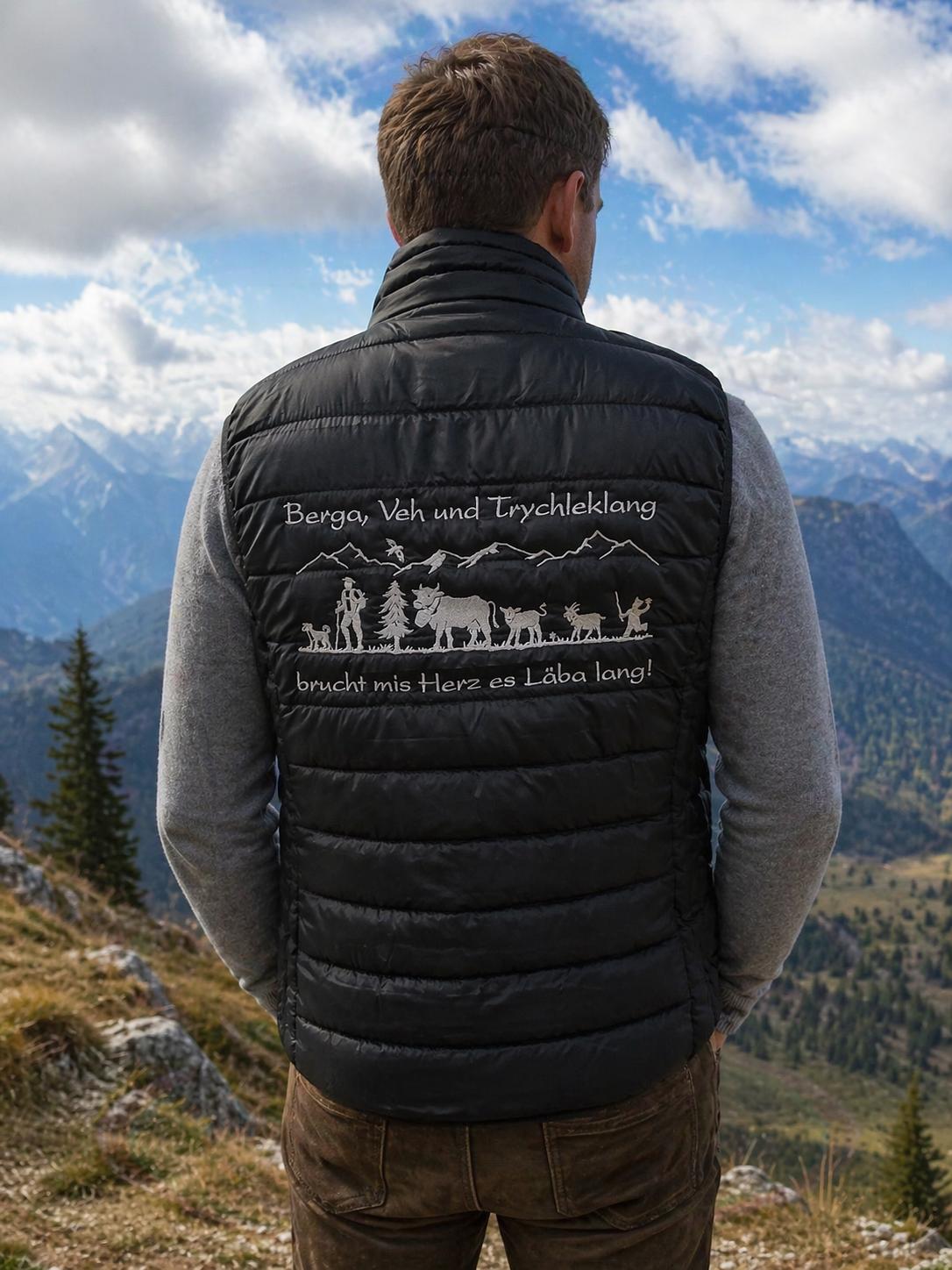 WhatsApp Image 2026-04-23 at 1026281 | fil - magic Stickerei Berther Man standing with his back to the camera on a mountain overlook, wearing a black quilted vest with an alpine scene and German text on the back.