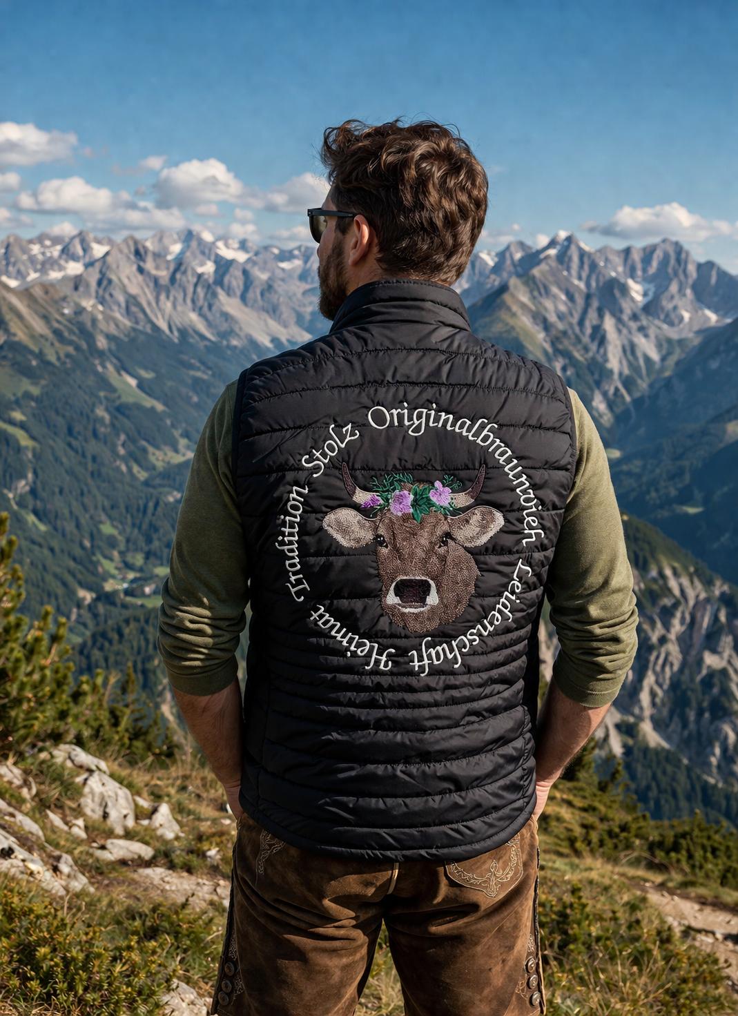 WhatsApp Image 2026-04-30 at 13523810 | fil - magic Stickerei Berther Man facing away on a mountain overlook, wearing a black quilted vest with a circular logo featuring a cow head and flowers; snowy peaks in the distance.