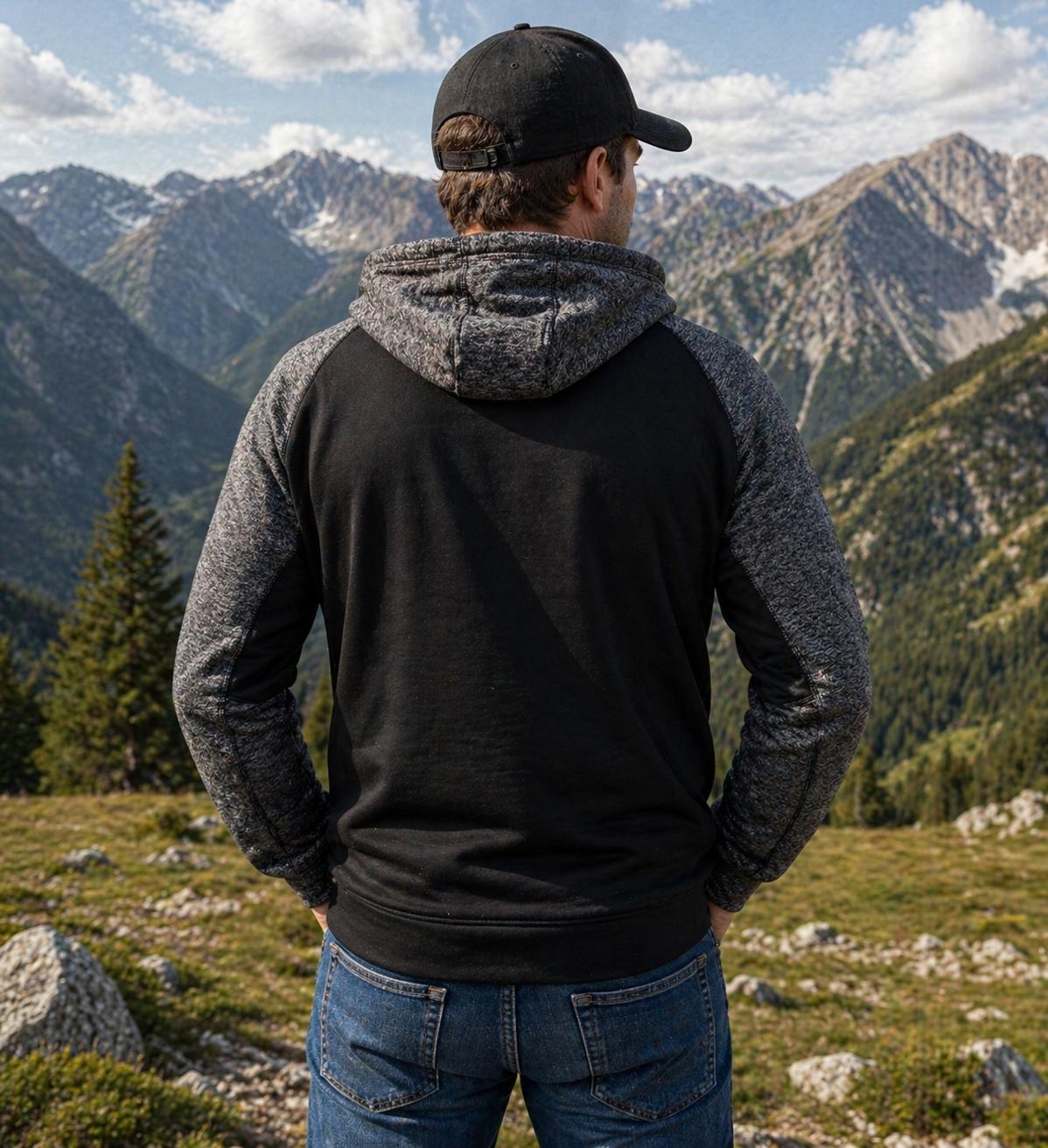 WhatsApp Image 2026-04-30 at 1352389 | fil - magic Stickerei Berther Man standing with back to camera, wearing a black and gray hooded sweatshirt and cap, overlooking rocky mountain landscape under a blue sky.