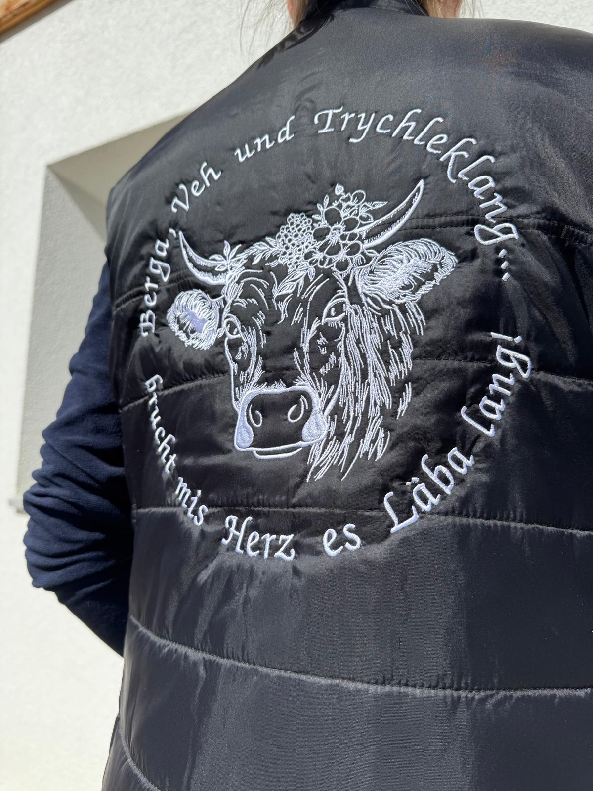 WhatsApp Image 2026-04-30 at 135352 | fil - magic Stickerei Berther Black quilted jacket back featuring a white embroidered cow head with a floral crown, encircled by German text punctuation-style around the design.