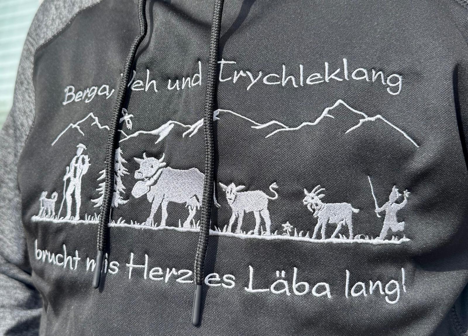 WhatsApp Image 2026-04-30 at 13535310 | fil - magic Stickerei Berther Black hoodie with white embroidery showing mountains, hikers, and goats, along a German slogan running across the top edge.