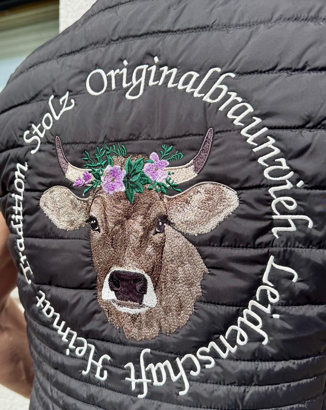 WhatsApp Image 2026-04-30 at 13535412 | fil - magic Stickerei Berther Embroidered cow head with a flower crown on a black quilted jacket, surrounded by white circular text.
