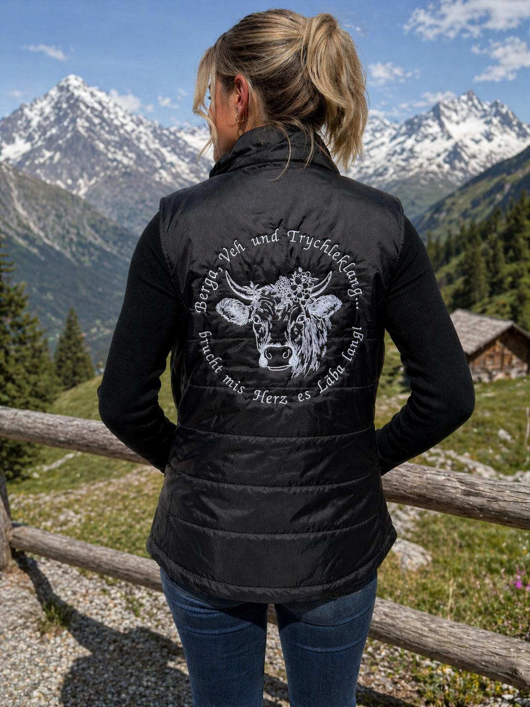 WhatsApp Image 2026-05-20 at 111440 | fil - magic Stickerei Berther Woman standing outdoors with back to camera, wearing a black padded vest with a white bull graphic and circular German text, in a mountainous landscape.
