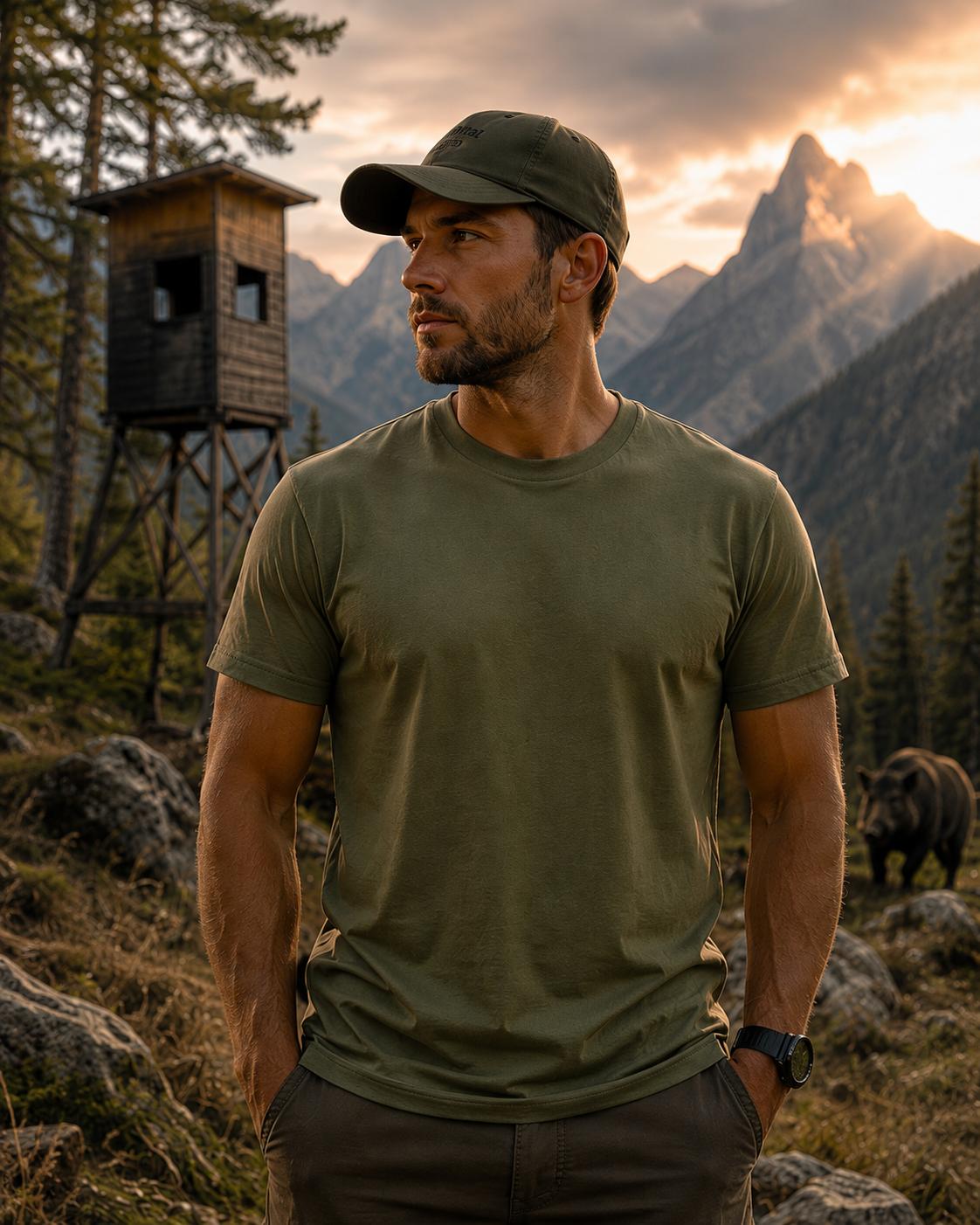 WhatsApp Image 2026-08-22 at 17280712 | fil - magic Stickerei Berther Man in olive green t-shirt and cap stands outdoors at sunset, with rugged mountains and a wooden lookout tower behind him.