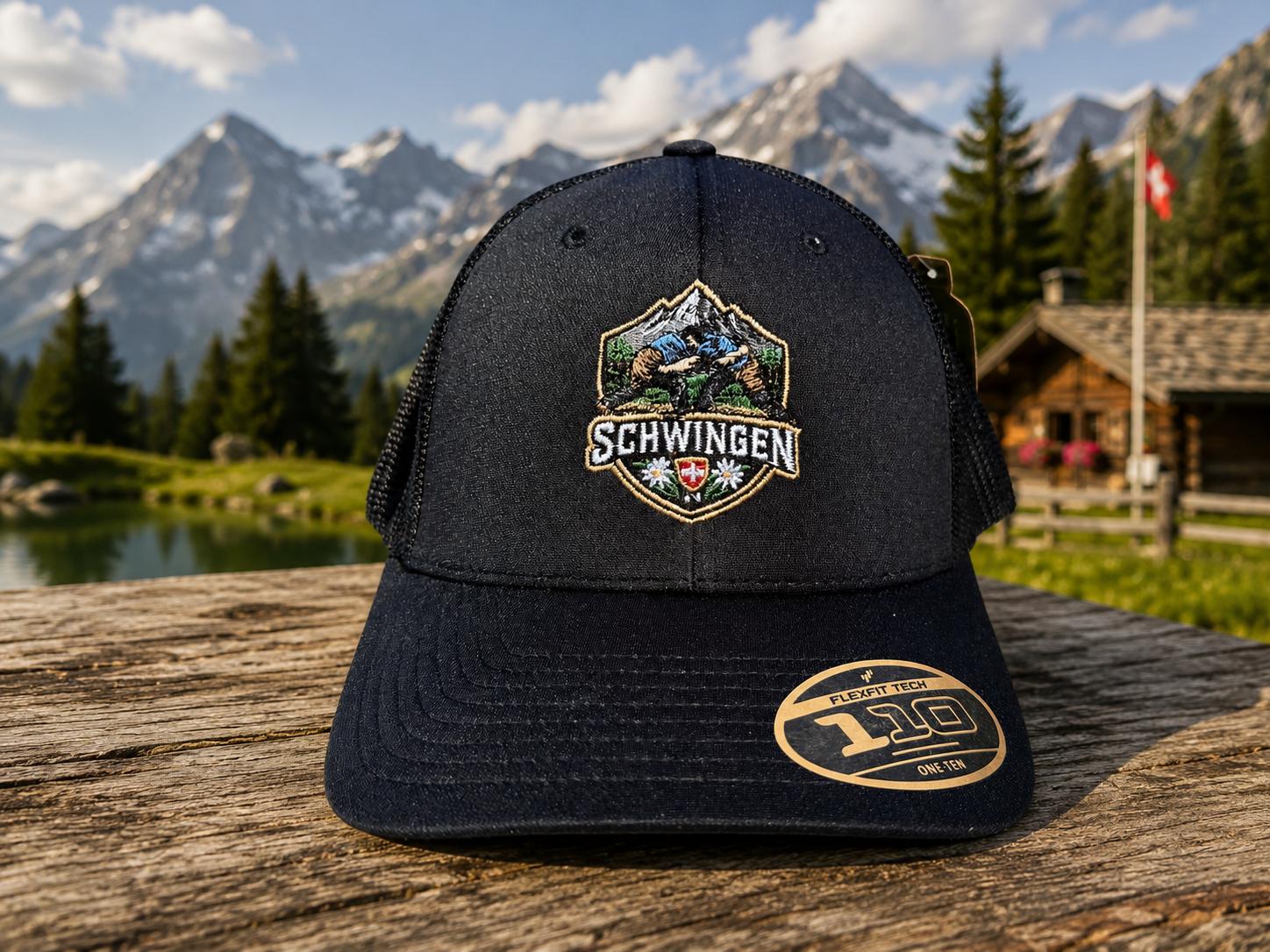 WhatsApp Image 2026-08-22 at 1728078 | fil - magic Stickerei Berther Black cap with a colorful embroidered badge reading SCHWINGEN, resting on a wooden table with alpine mountains in the background.